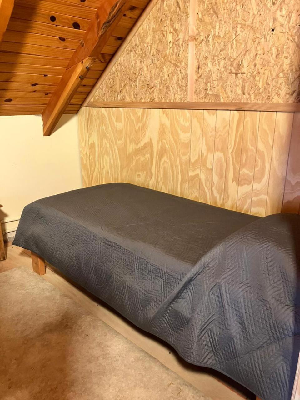 Single bed with a grey bedspread by the wooden wall