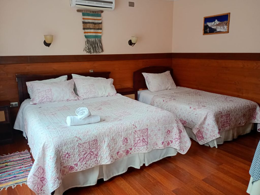 Habitación con cama matrimonial, cama individual, zócalo de madera y aire acondicionado