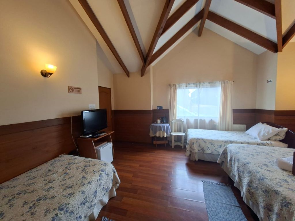 Habitación con tres camas individuales, piso de madera y ventana con cortinas