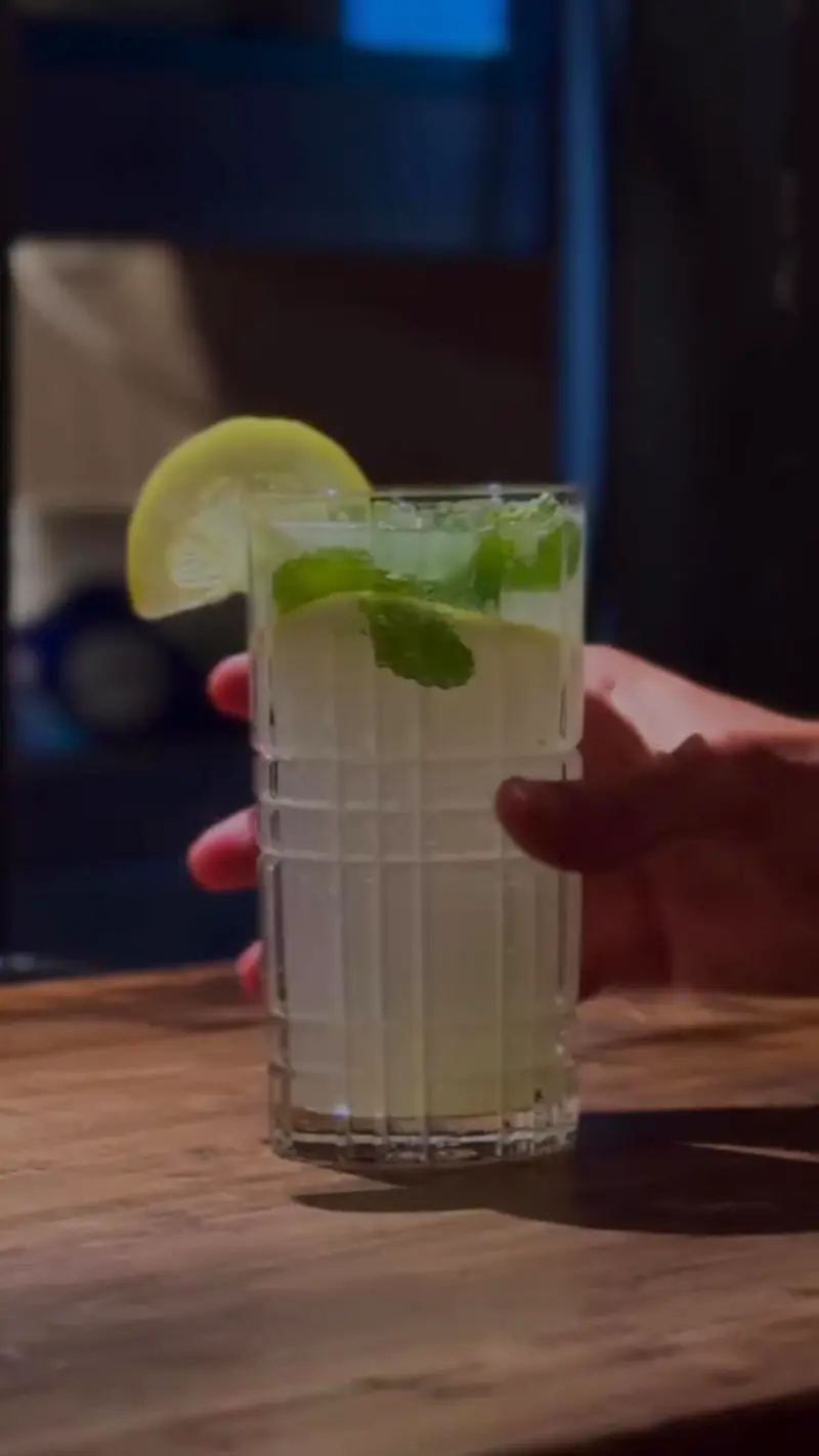 Vaso alto con una bebida fresca, lima y hojas de menta sobre una mesa de madera