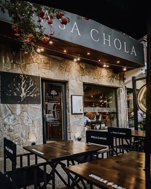 Frente de piedra de Casa Chola con el logo y mesas de madera en la vereda