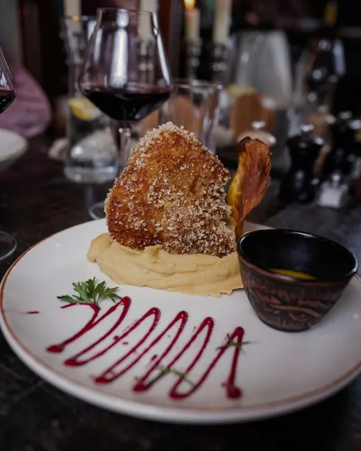 Copa de vino tinto junto a un plato de la casa, con velas al fondo