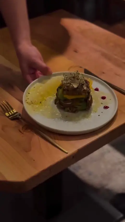 Un mozo apoya un plato de autor sobre una mesa de madera