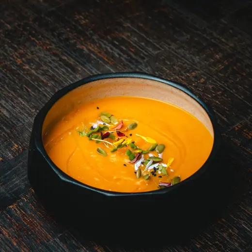 Sopa de calabaza y jengibre en un bowl negro, con semillas y brotes por encima