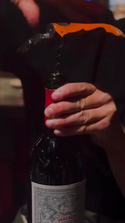 Manos descorchando una botella de vino tinto