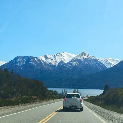 Camioneta plateada por la ruta de montaña con la cordillera nevada de fondo