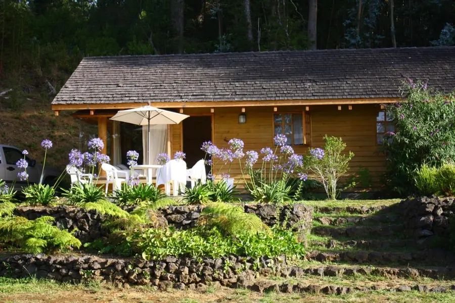 Cabaña de madera con terraza y sombrilla rodeada de flores