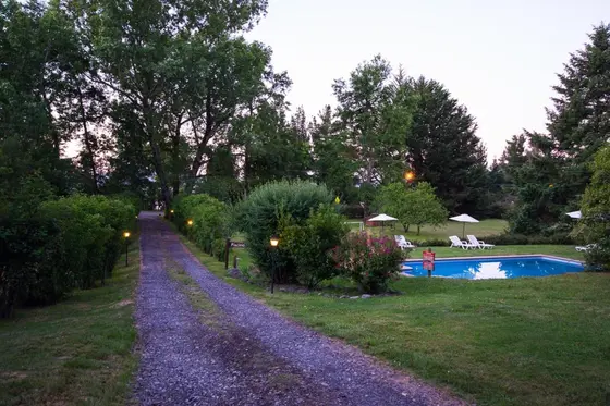 Camino de tierra bordeado de jardines con la piscina al fondo