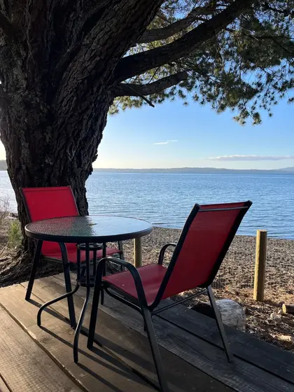 Mesa con dos sillas rojas bajo un pino, frente al lago Villarrica