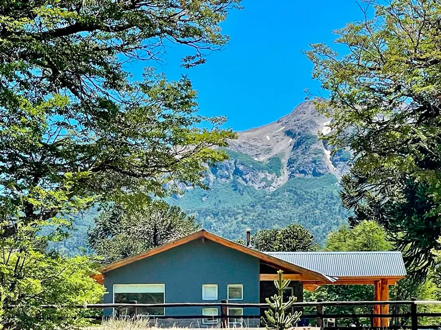 Una cabaña enmarcada por los árboles, con el cerro detrás