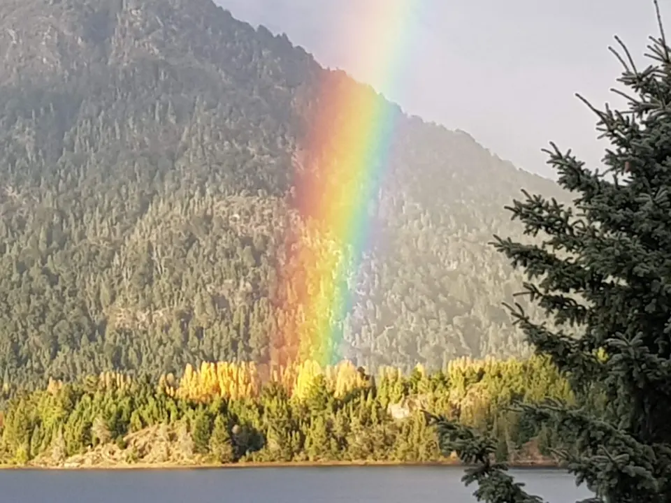 Un arco iris cae sobre el bosque de otoño, frente al lago