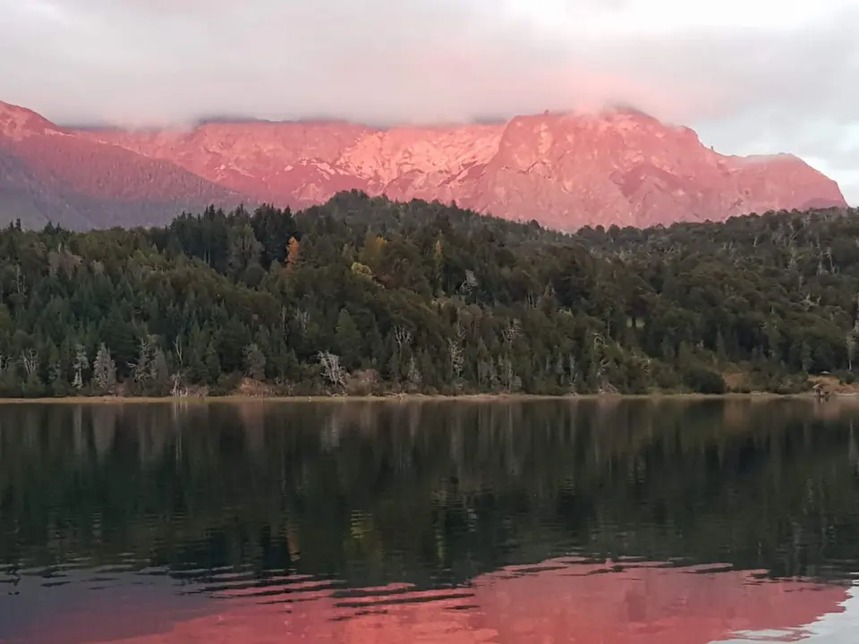 El cerro encendido de rosa al atardecer, reflejado en el lago