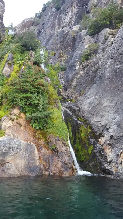 Una cascada cae sobre el lago entre rocas y musgo