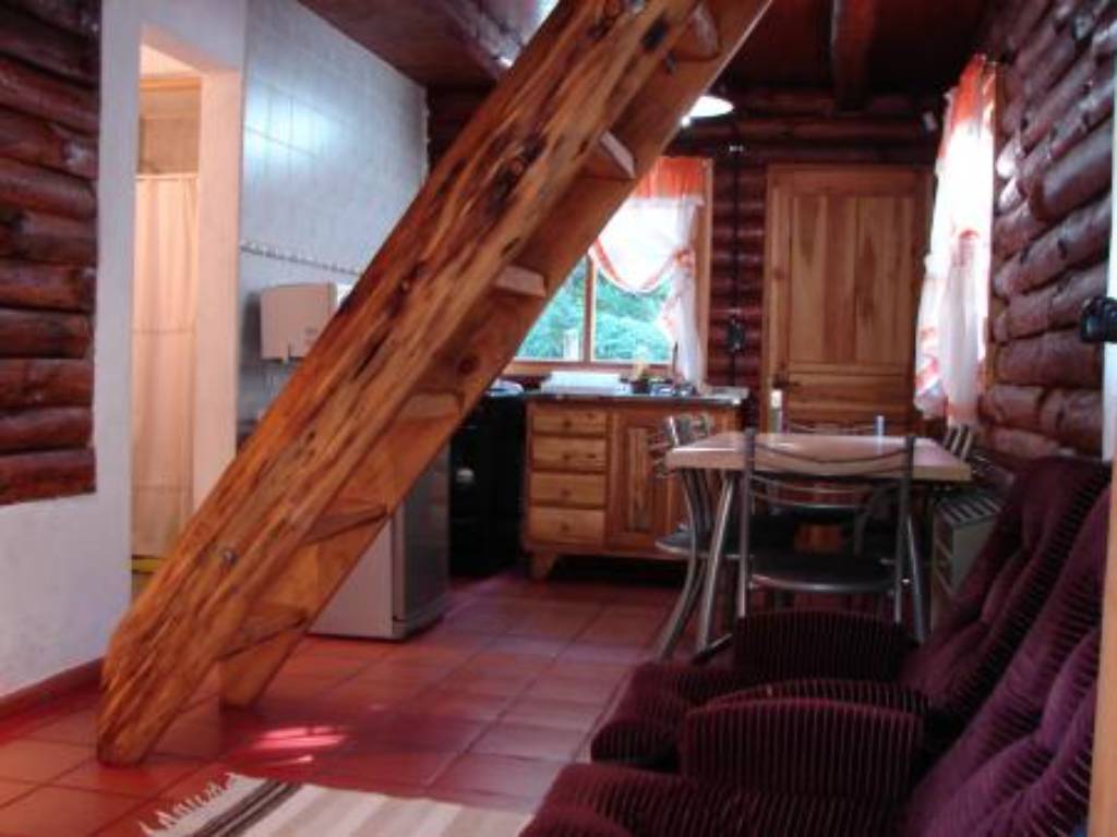 Estar y cocina de una cabaña, con escalera de madera al entrepiso