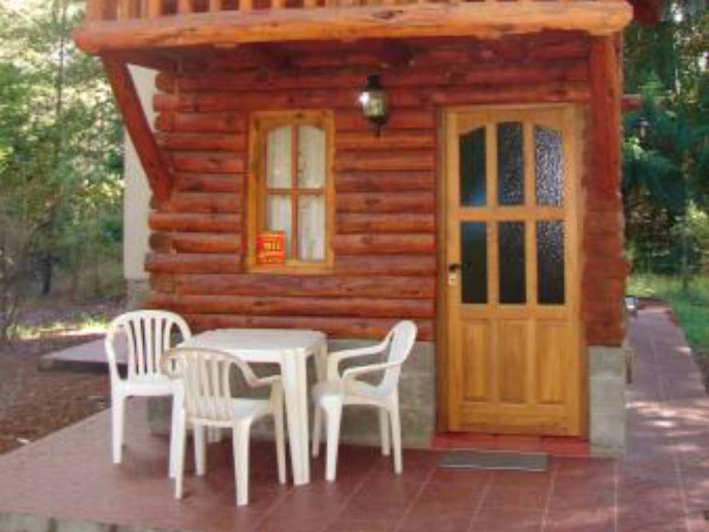 Entrada de una cabaña de troncos con mesa y sillas afuera