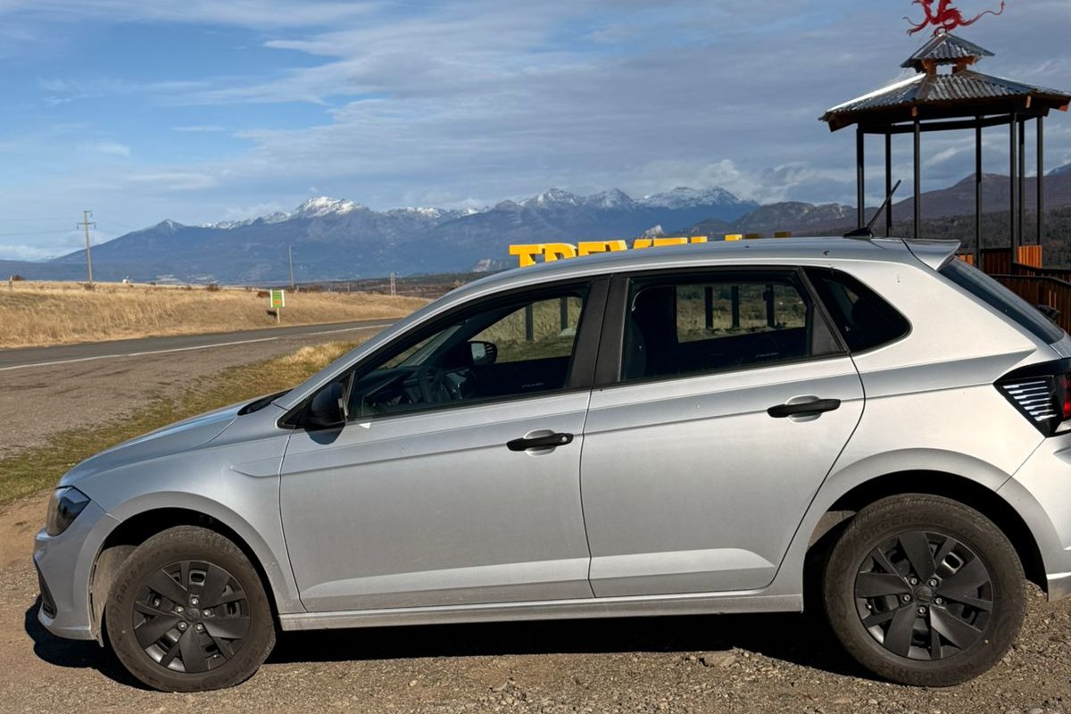 Volkswagen Polo gris de la flota junto al cartel de Trevelin, con la cordillera de fondo